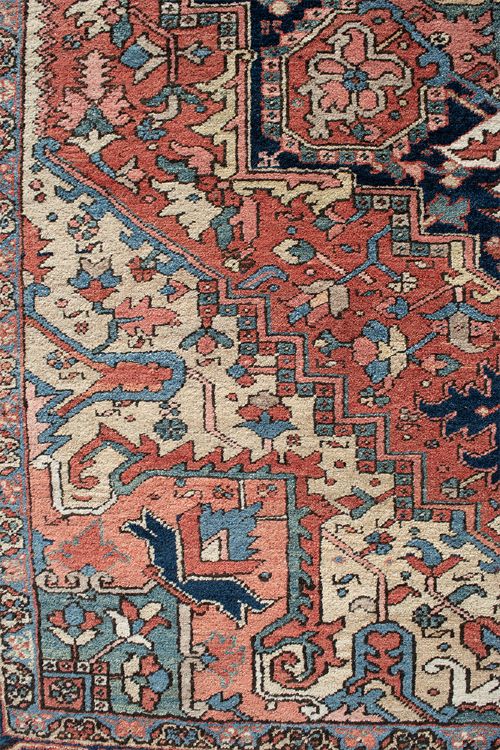 An antique Persian Heriz wool carpet with a large central geometric medallion in terracotta, navy blue, and light blue against an ivory and red field. View VI