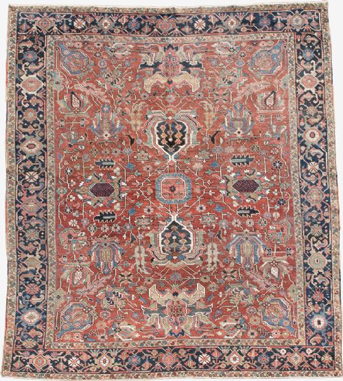 An antique Persian Heriz wool carpet featuring a central geometric medallion on a terracotta field surrounded by a dark navy decorative border. View X