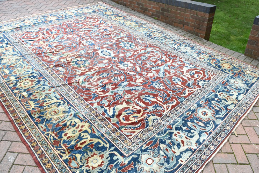 A large hand-knotted Persian wool carpet featuring a terracotta ground decorated with elaborate blue and ivory floral arabesques framed by an indigo border.