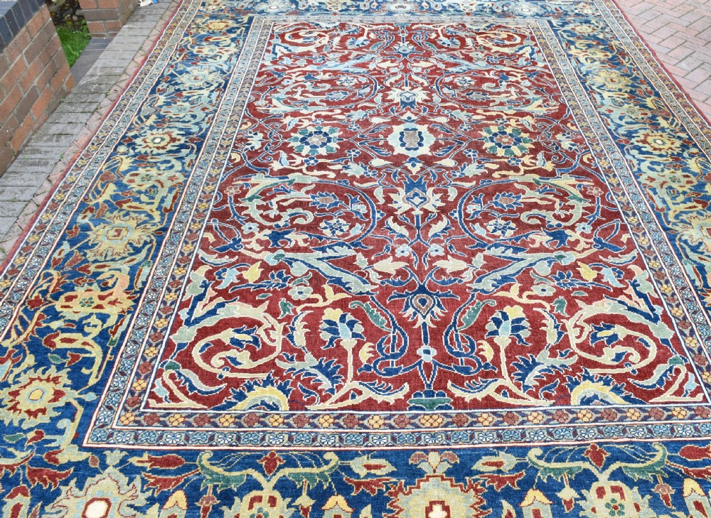 A large hand-knotted Persian wool carpet featuring a terracotta ground decorated with elaborate blue and ivory floral arabesques framed by an indigo border. View III