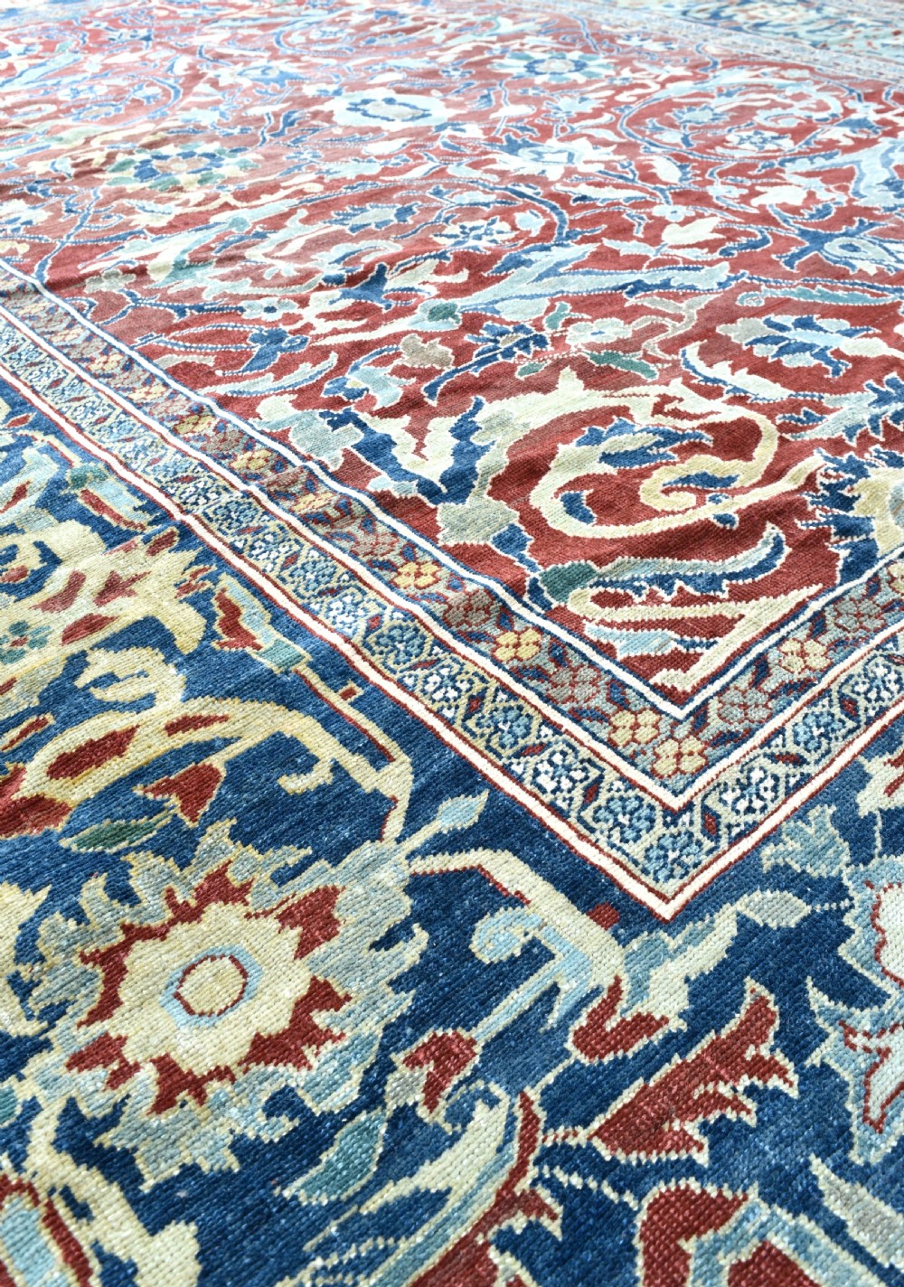 A large hand-knotted Persian wool carpet featuring a terracotta ground decorated with elaborate blue and ivory floral arabesques framed by an indigo border. View IV