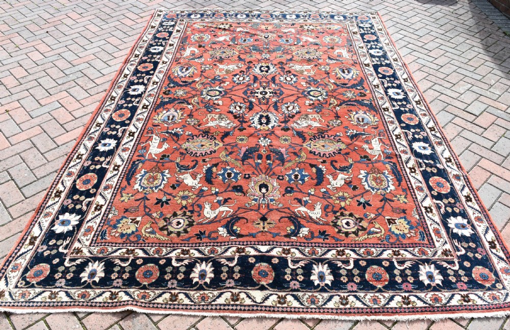 A large hand-knotted antique Persian Veramin carpet featuring animal and floral motifs on a terracotta field with a dark navy border.