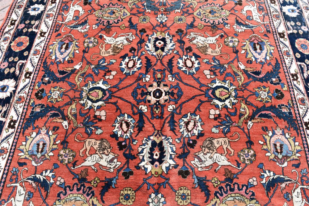 A large hand-knotted antique Persian Veramin carpet featuring animal and floral motifs on a terracotta field with a dark navy border. View II