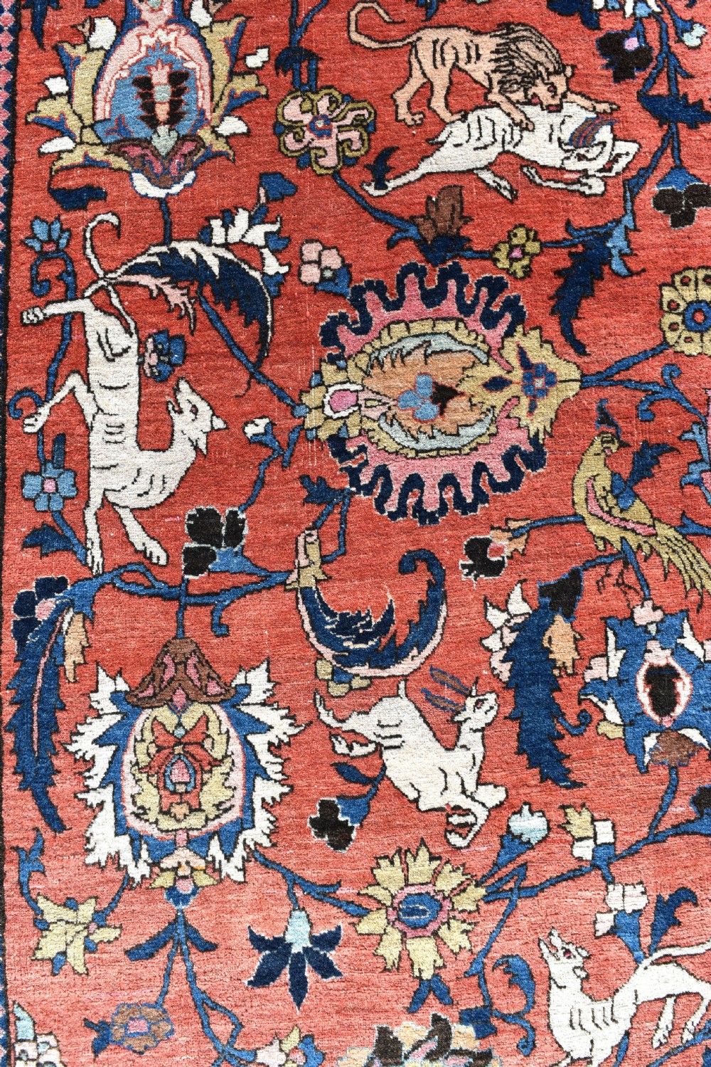 A large hand-knotted antique Persian Veramin carpet featuring animal and floral motifs on a terracotta field with a dark navy border. View III