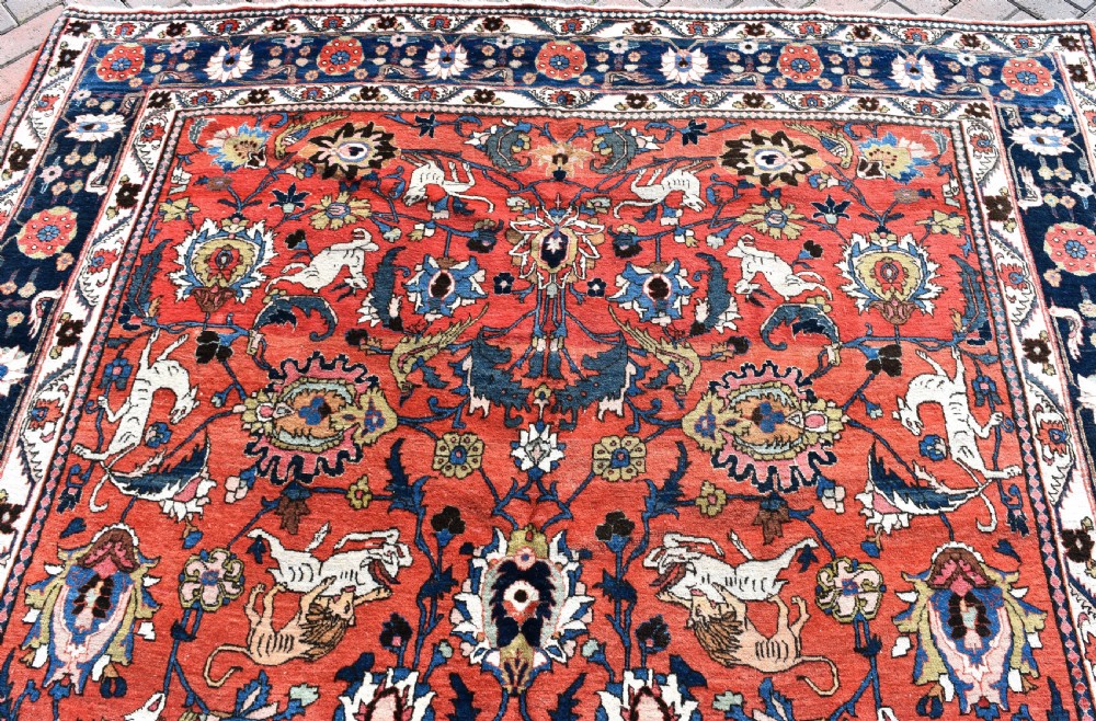 A large hand-knotted antique Persian Veramin carpet featuring animal and floral motifs on a terracotta field with a dark navy border. View IV