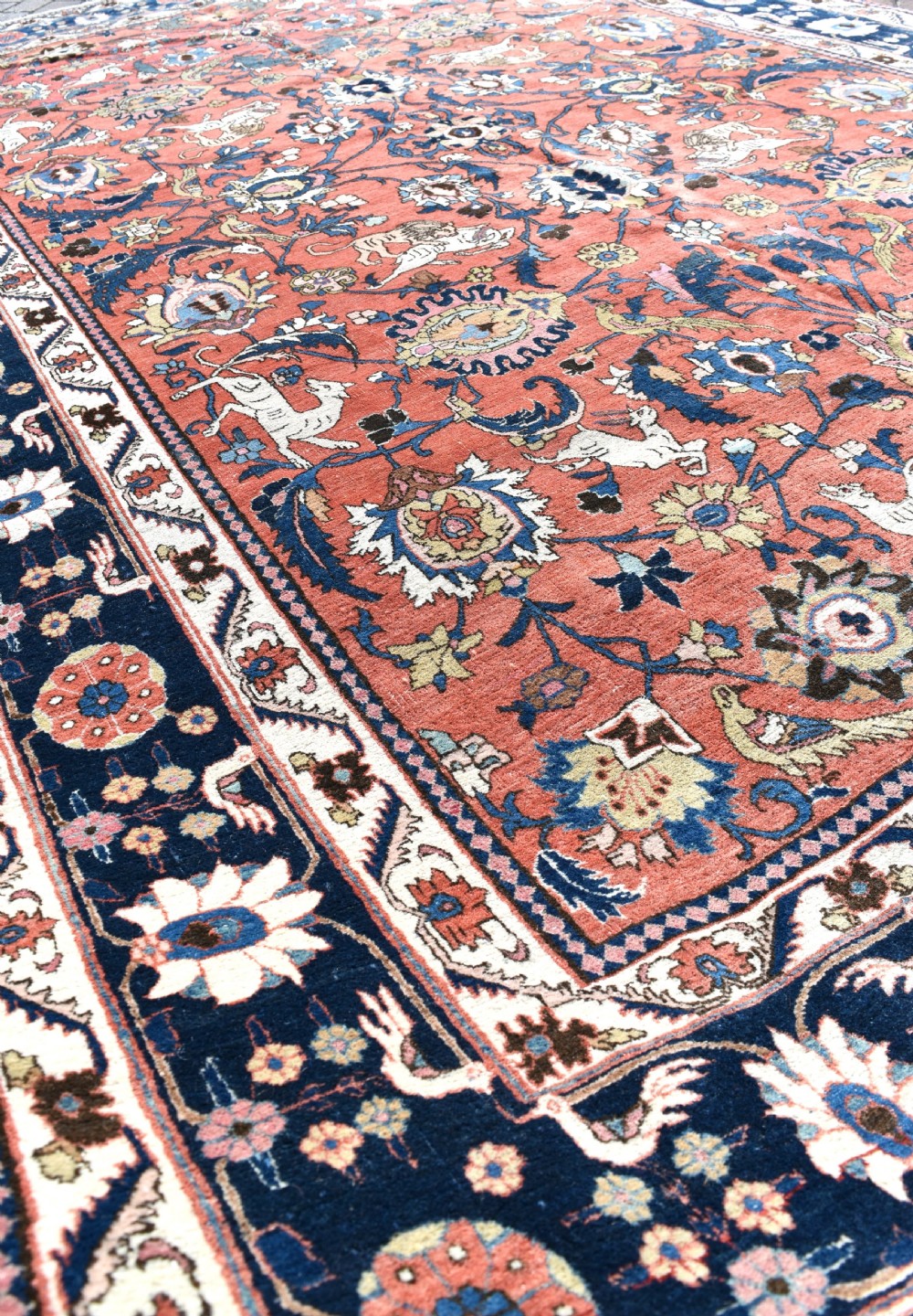 A large hand-knotted antique Persian Veramin carpet featuring animal and floral motifs on a terracotta field with a dark navy border. View V