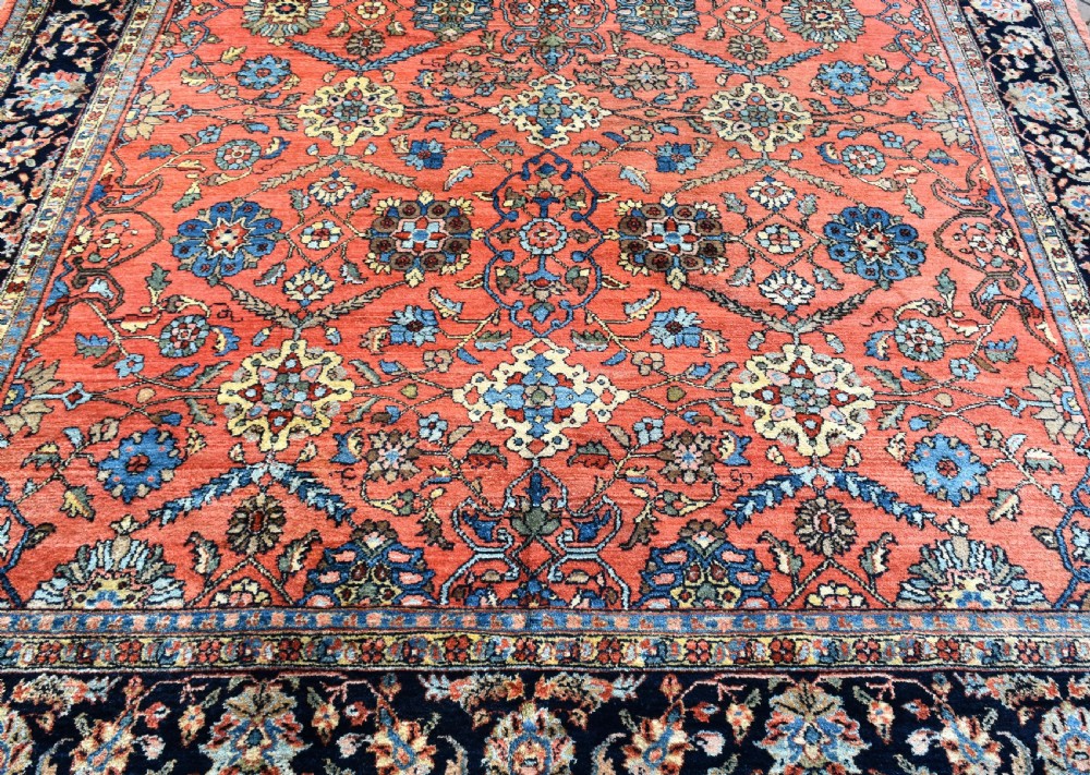 An antique Persian Lilihan wool carpet featuring a terracotta pink field woven with blue floral motifs and framed by a dark navy ornate border. View III