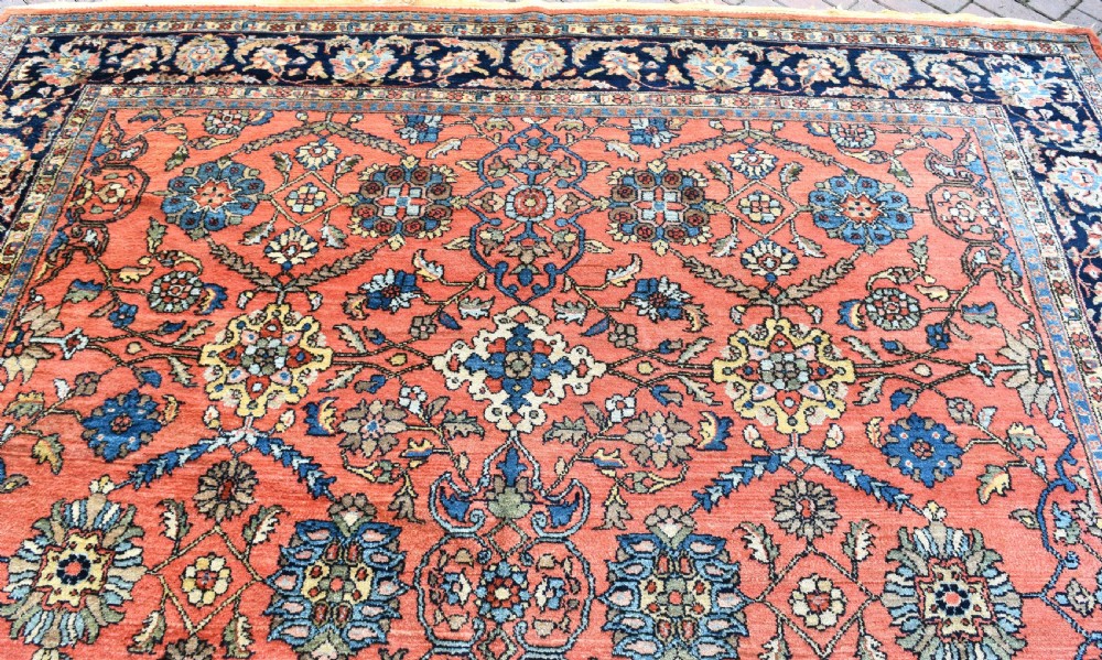 An antique Persian Lilihan wool carpet featuring a terracotta pink field woven with blue floral motifs and framed by a dark navy ornate border. View IV