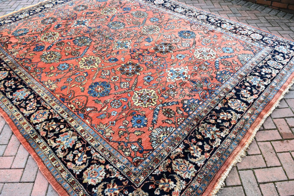 An antique Persian Lilihan wool carpet featuring a terracotta pink field woven with blue floral motifs and framed by a dark navy ornate border. View VI