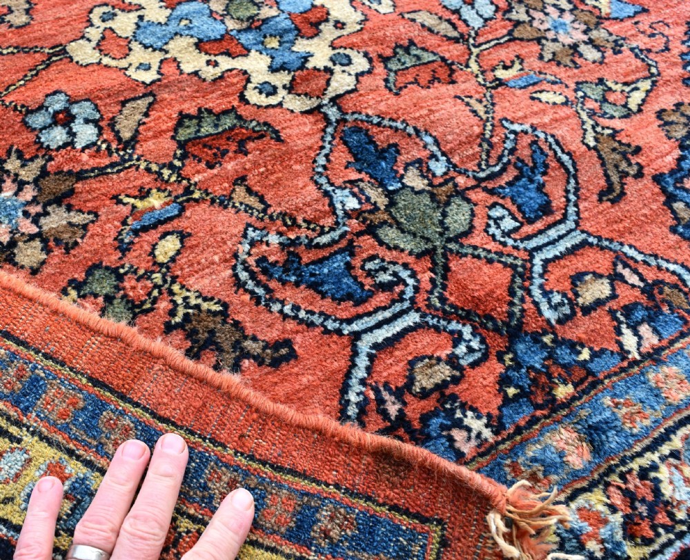 An antique Persian Lilihan wool carpet featuring a terracotta pink field woven with blue floral motifs and framed by a dark navy ornate border. View VIII