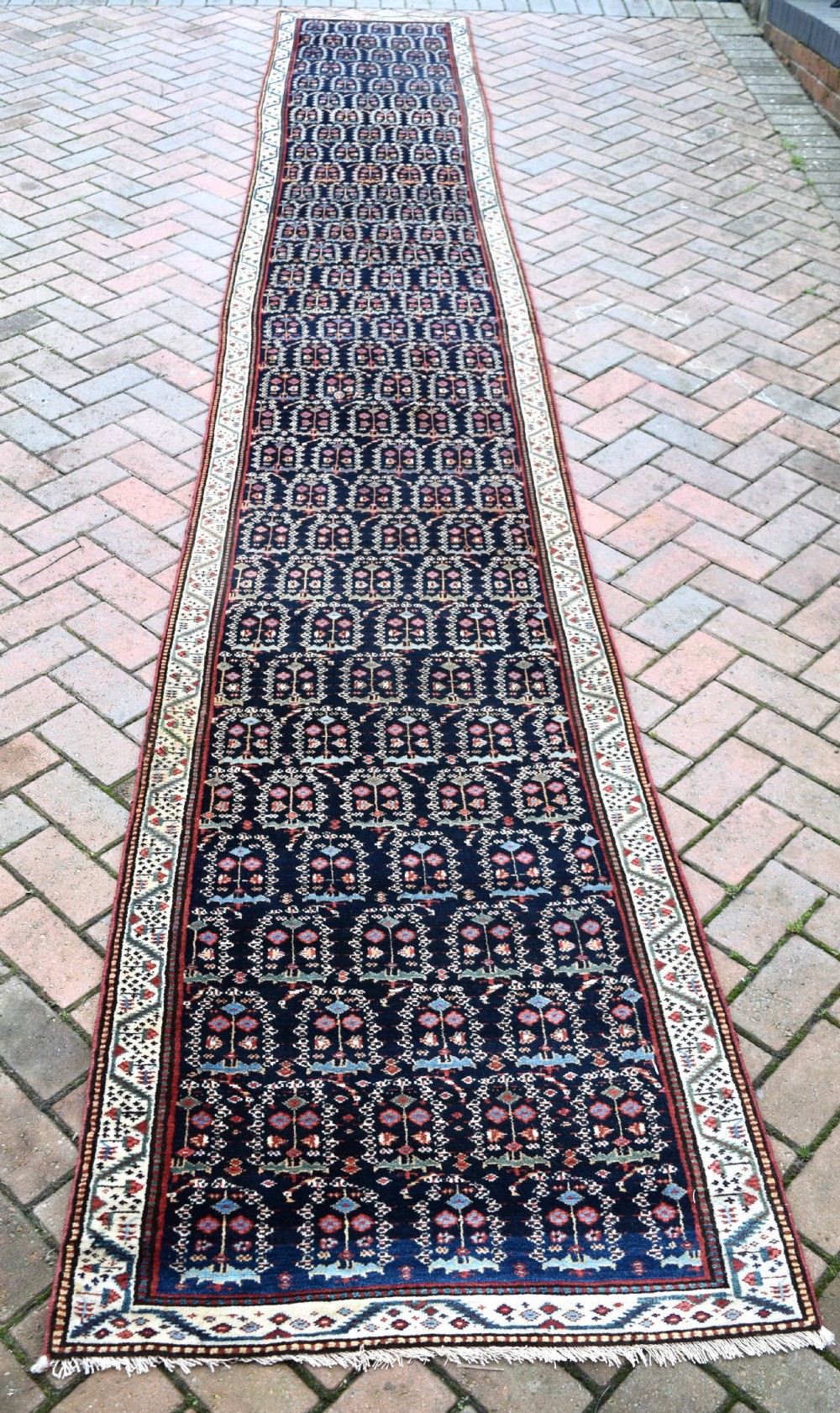 An antique Northwest Persian wool runner rug featuring repeating geometric shrub motifs on a navy blue field framed by a cream border.