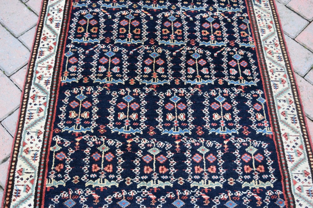 An antique Northwest Persian wool runner rug featuring repeating geometric shrub motifs on a navy blue field framed by a cream border. View V