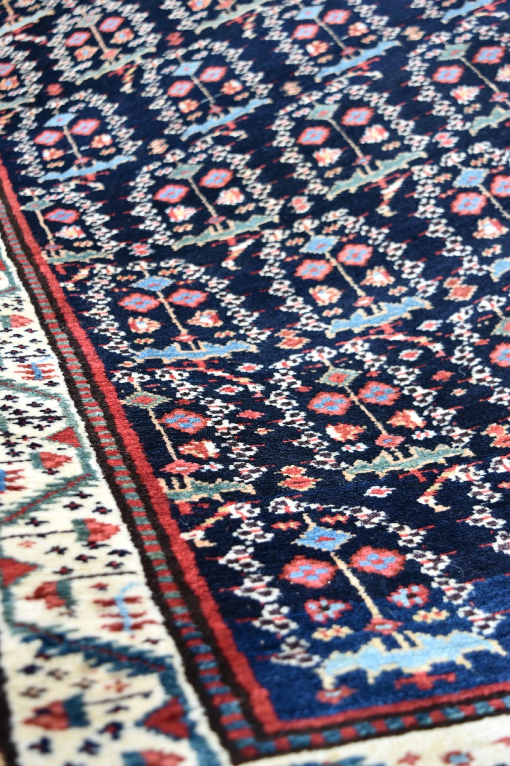 An antique Northwest Persian wool runner rug featuring repeating geometric shrub motifs on a navy blue field framed by a cream border. View X