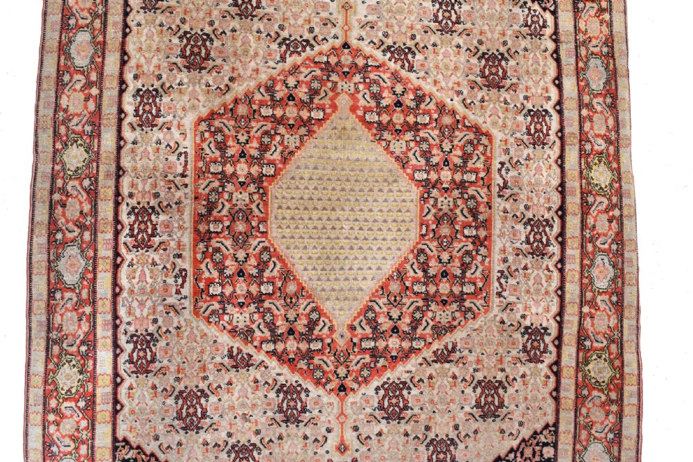 An antique Persian Senneh hand-knotted wool rug featuring a central cream stepped medallion surrounded by intricate red and blue geometric borders. View III
