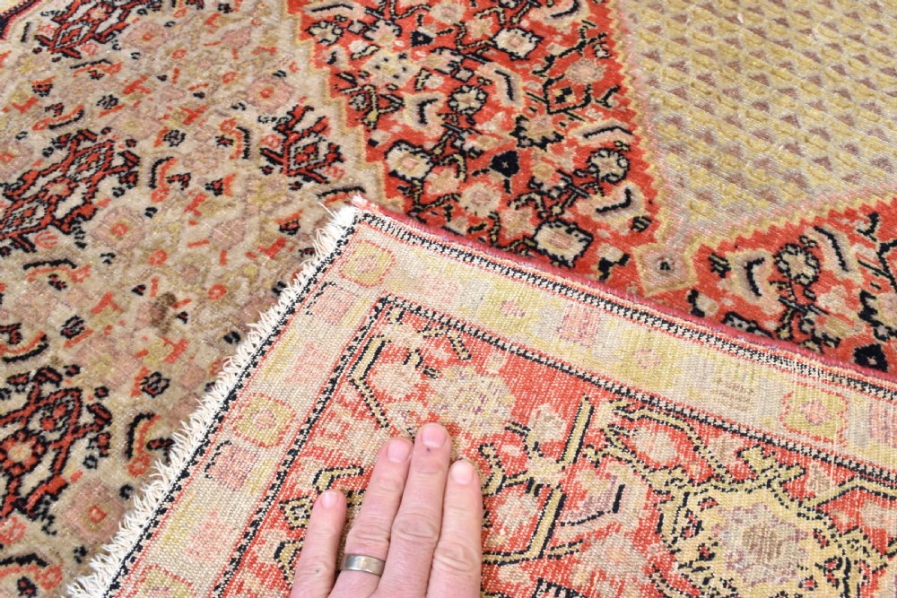 An antique Persian Senneh hand-knotted wool rug featuring a central cream stepped medallion surrounded by intricate red and blue geometric borders. View IV