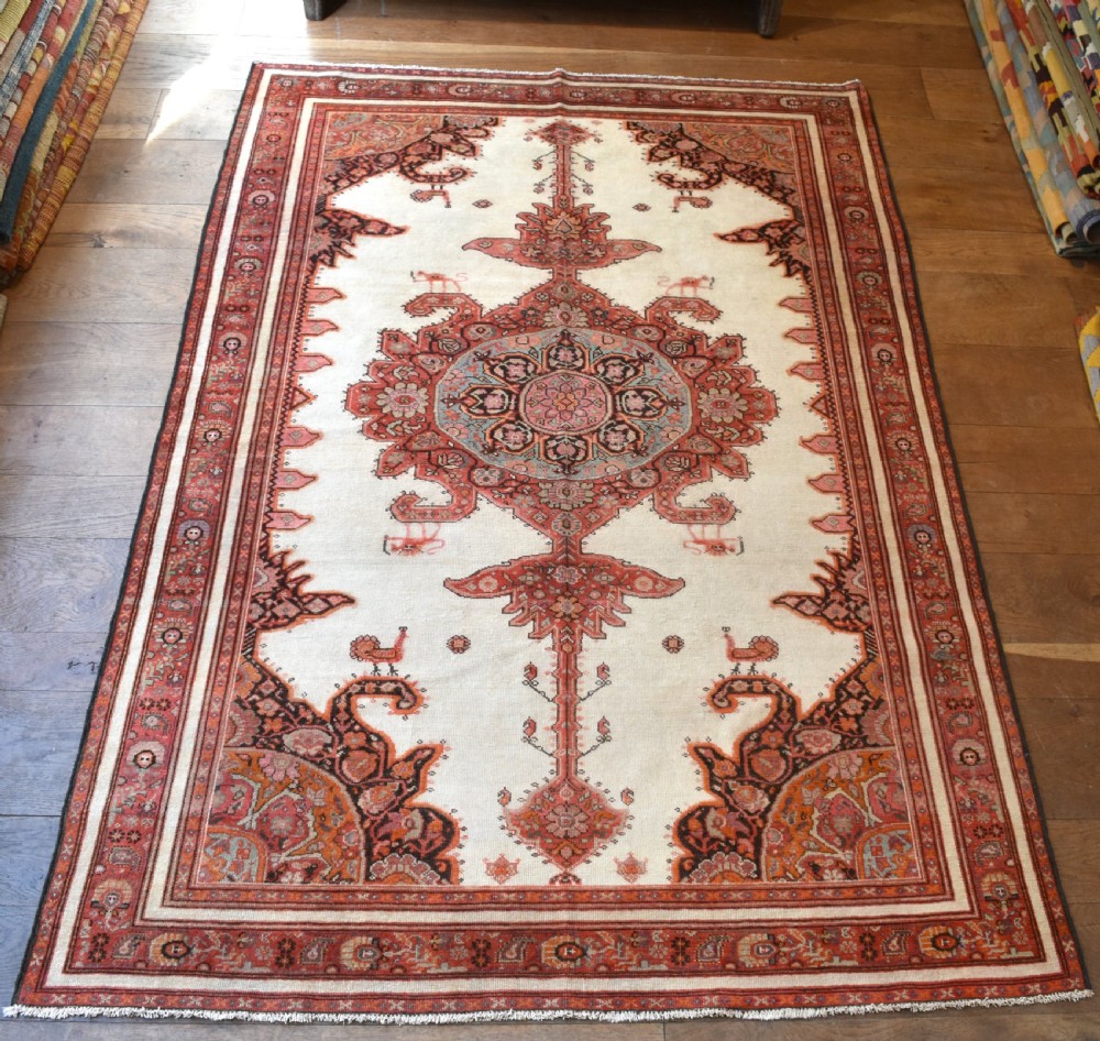 An antique Persian Malayer hand-knotted wool rug featuring a central stepped medallion, stylized lion motifs, and an ivory field framed by terracotta borders.