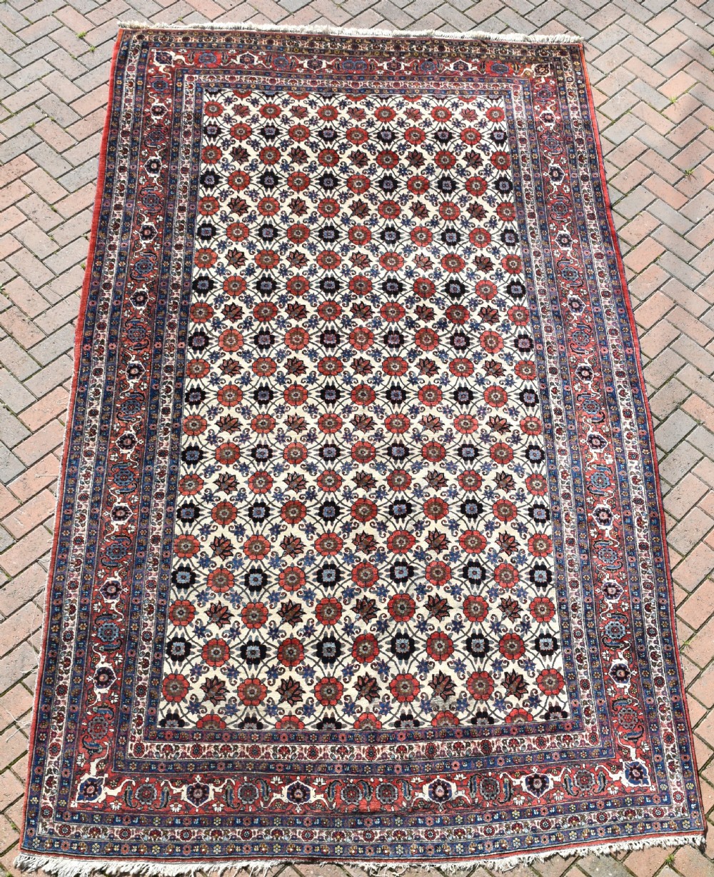 An antique Persian Veramin hand-knotted wool carpet featuring a repeating floral trellis pattern on an ivory field surrounded by multi-band borders.