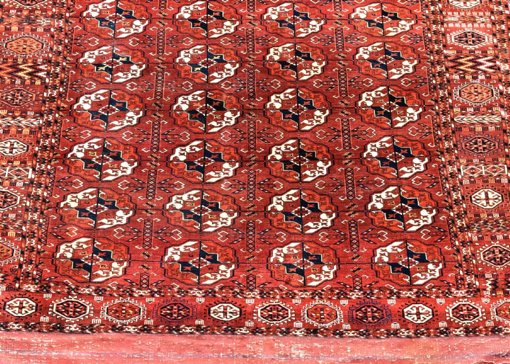 An antique hand-knotted Tekke Turkmen wool main carpet featuring repeating geometric gul motifs on a deep terracotta red field with decorative borders and flatweave ends. View II