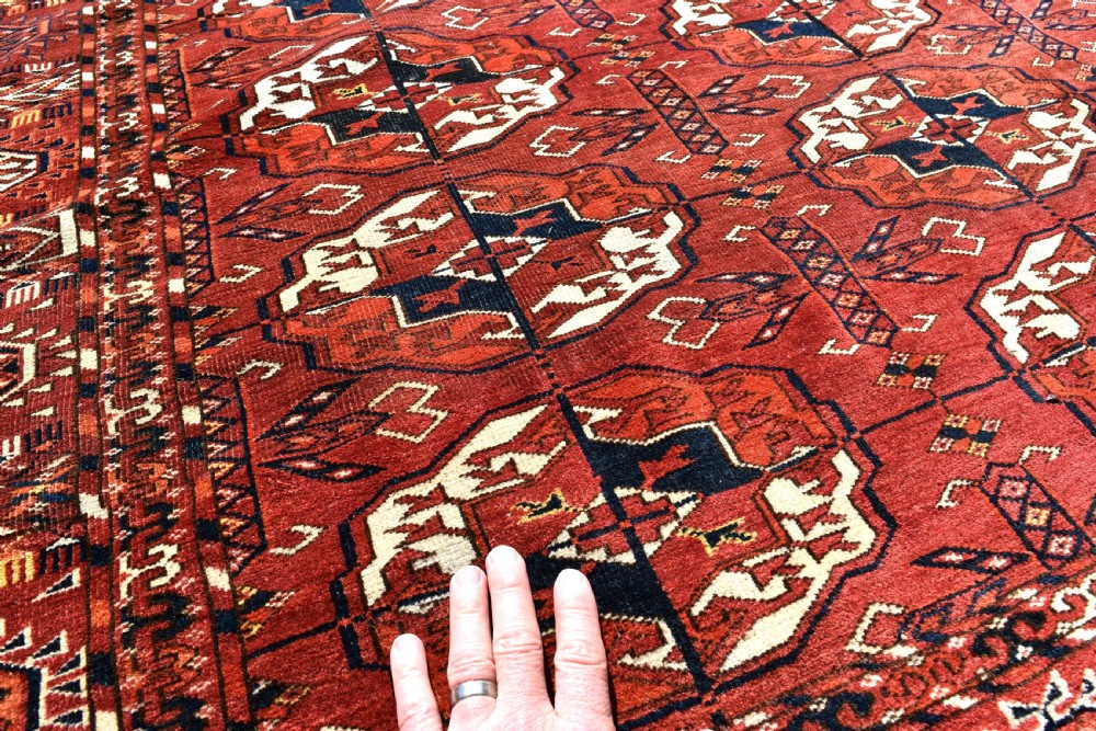 An antique hand-knotted Tekke Turkmen wool main carpet featuring repeating geometric gul motifs on a deep terracotta red field with decorative borders and flatweave ends. View III