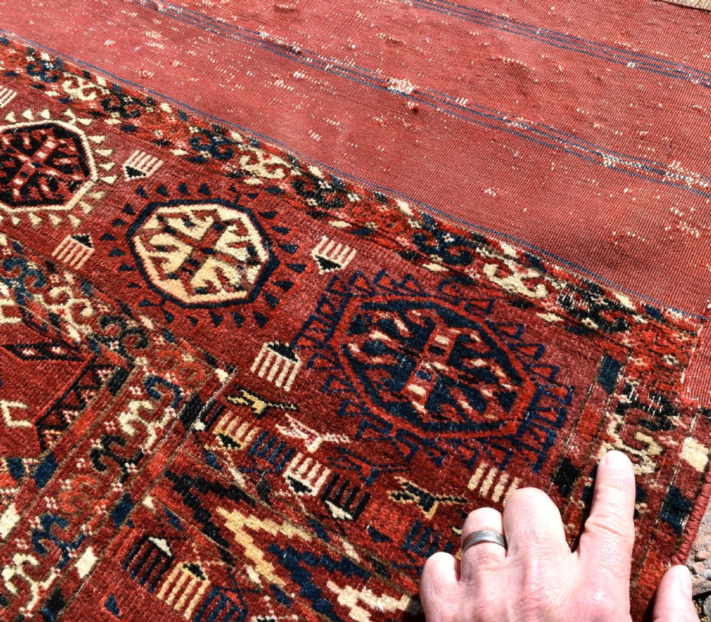 An antique hand-knotted Tekke Turkmen wool main carpet featuring repeating geometric gul motifs on a deep terracotta red field with decorative borders and flatweave ends. View IV