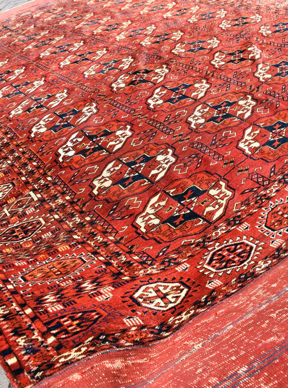 An antique hand-knotted Tekke Turkmen wool main carpet featuring repeating geometric gul motifs on a deep terracotta red field with decorative borders and flatweave ends. View VI