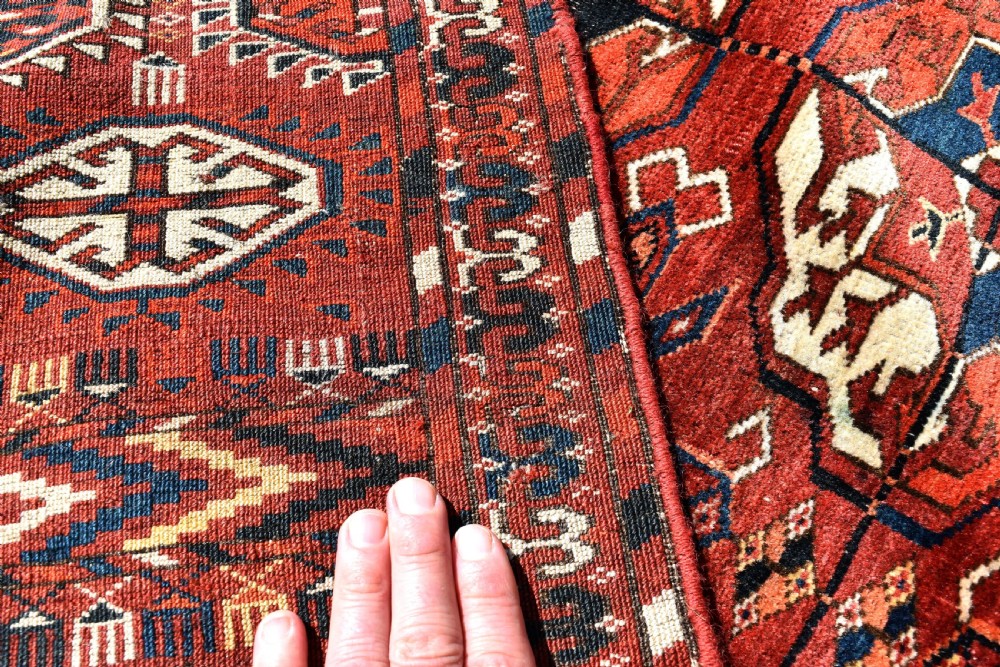 An antique hand-knotted Tekke Turkmen wool main carpet featuring repeating geometric gul motifs on a deep terracotta red field with decorative borders and flatweave ends. View VII