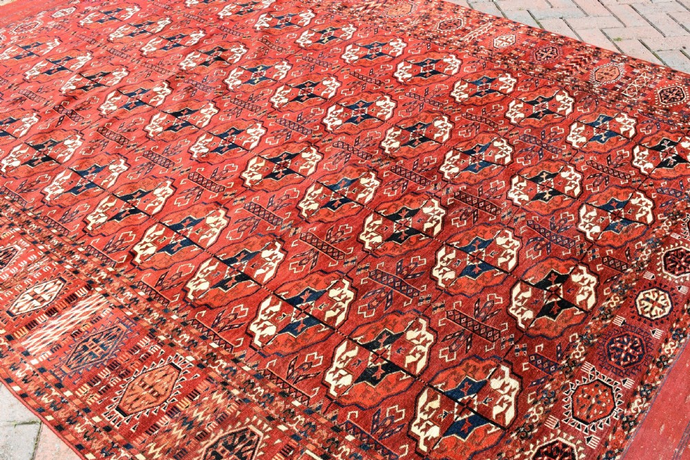 An antique hand-knotted Tekke Turkmen wool main carpet featuring repeating geometric gul motifs on a deep terracotta red field with decorative borders and flatweave ends. View VIII