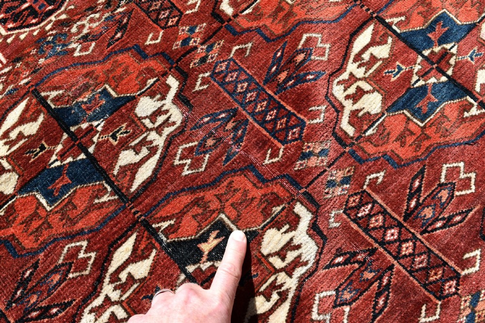 An antique hand-knotted Tekke Turkmen wool main carpet featuring repeating geometric gul motifs on a deep terracotta red field with decorative borders and flatweave ends. View IX