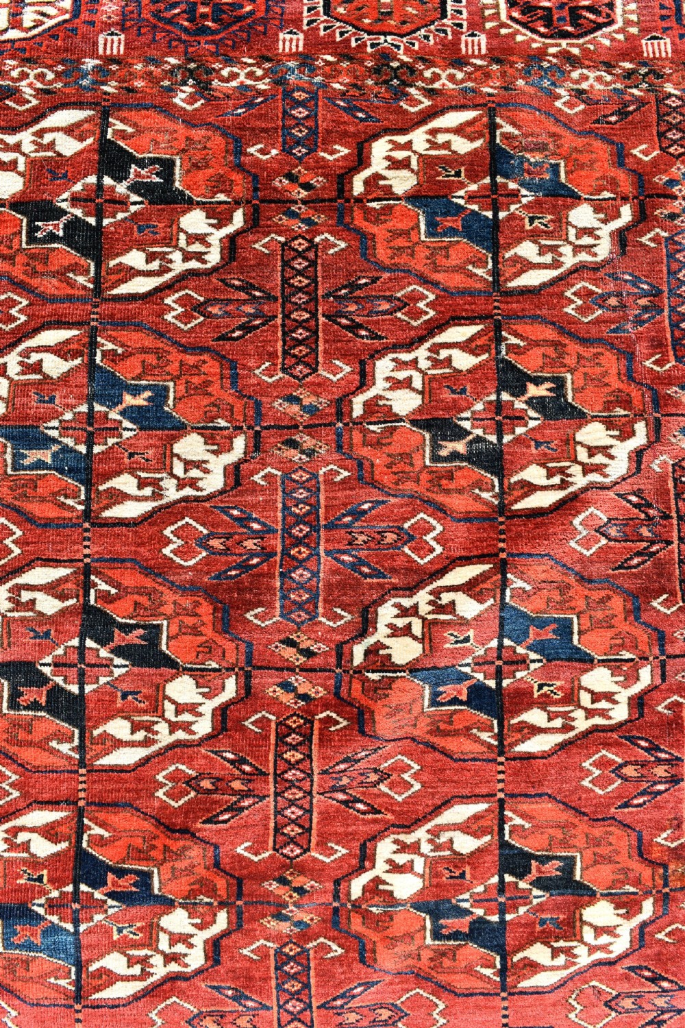 An antique hand-knotted Tekke Turkmen wool main carpet featuring repeating geometric gul motifs on a deep terracotta red field with decorative borders and flatweave ends. View X