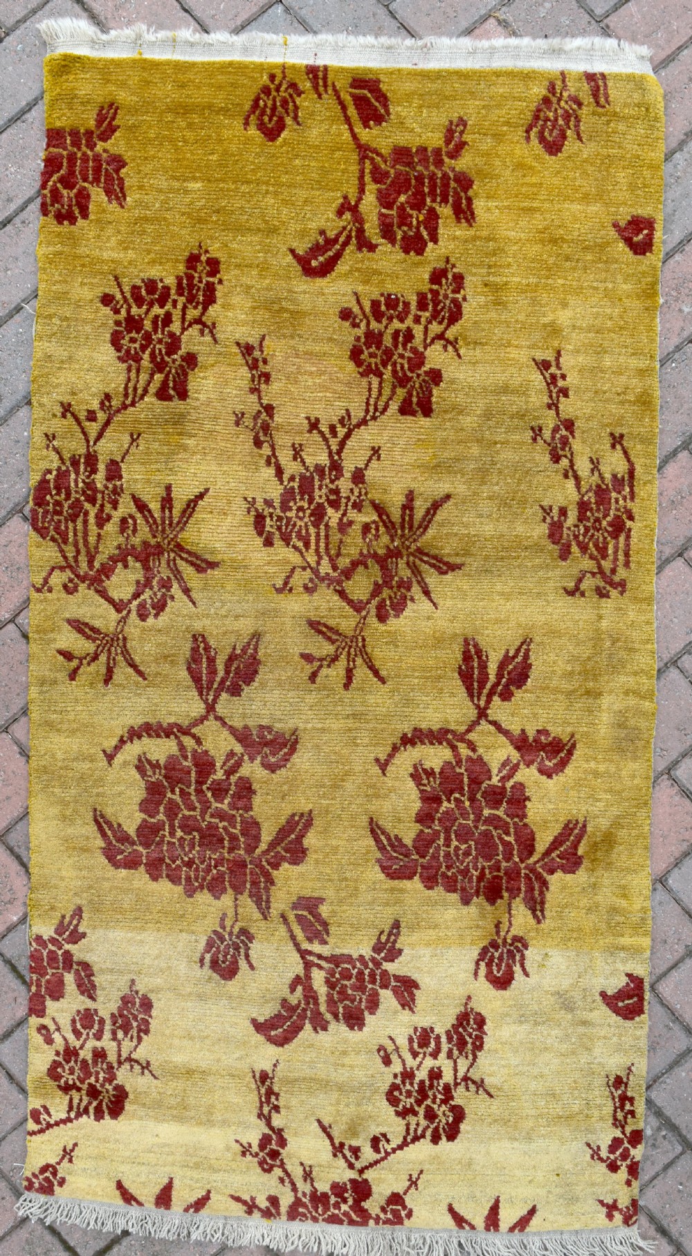 An antique rectangular Tibetan Khaden wool rug featuring a yellow field decorated with crimson floral branch motifs and fringe along the top and bottom edges.