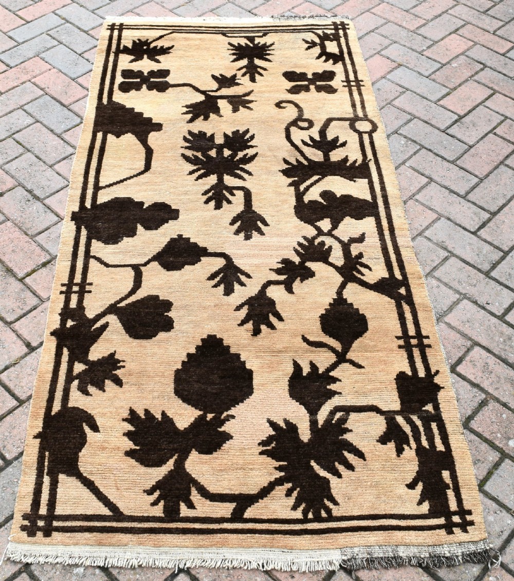 An antique Tibetan khaden rug featuring dark brown botanical motifs against a beige background, displayed flat on paved ground.