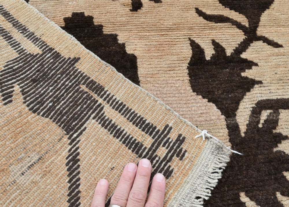 An antique Tibetan khaden rug featuring dark brown botanical motifs against a beige background, displayed flat on paved ground. View IV