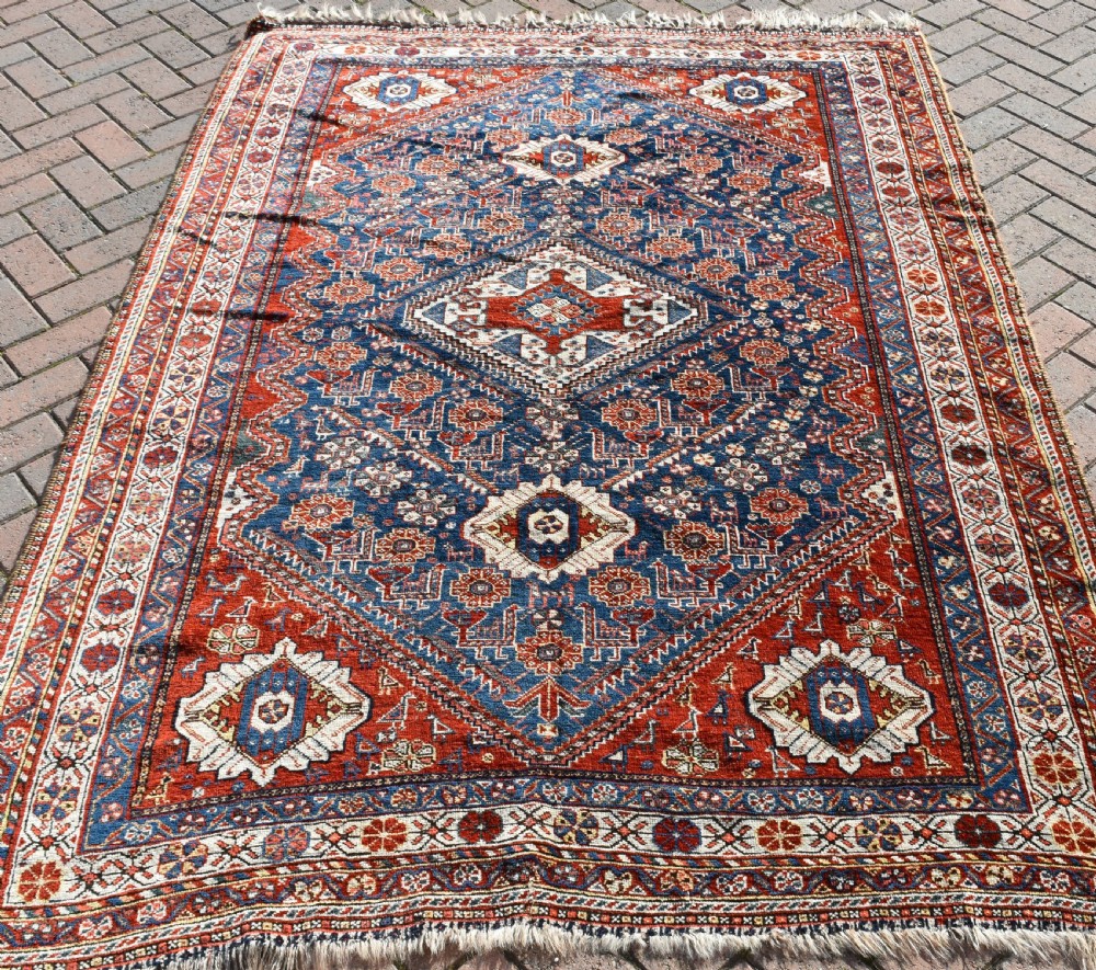 An antique Qashqai tribal wool rug with geometric diamond medallions in navy blue, terracotta red, and cream with fringed edges. View II