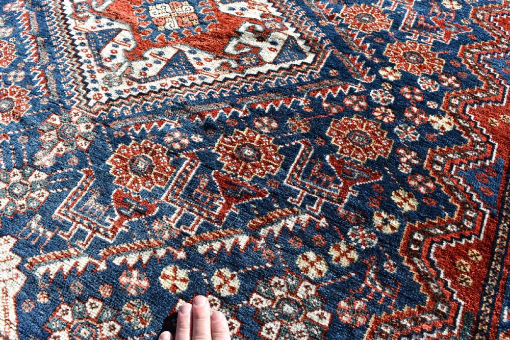 An antique Qashqai tribal wool rug with geometric diamond medallions in navy blue, terracotta red, and cream with fringed edges. View VI