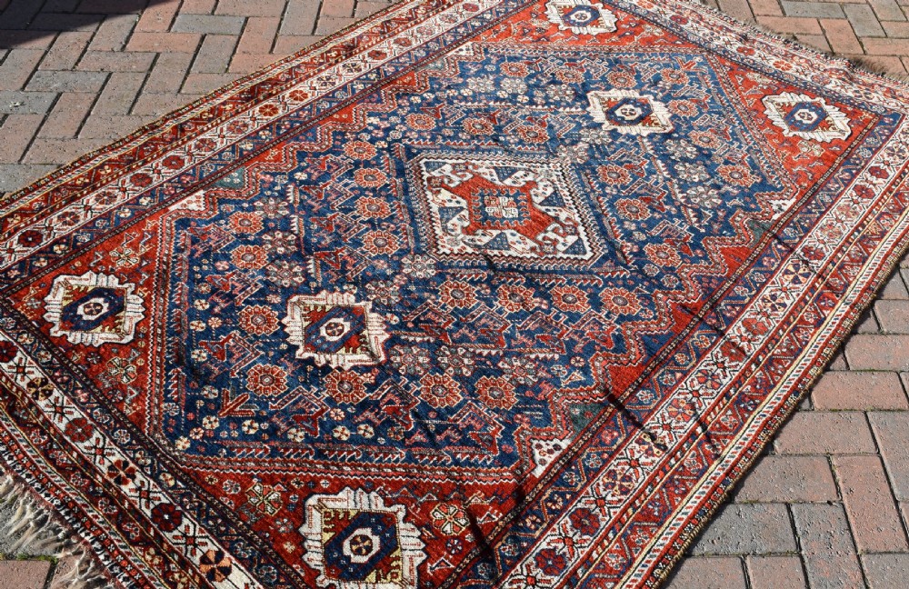 An antique Qashqai tribal wool rug with geometric diamond medallions in navy blue, terracotta red, and cream with fringed edges. View VII
