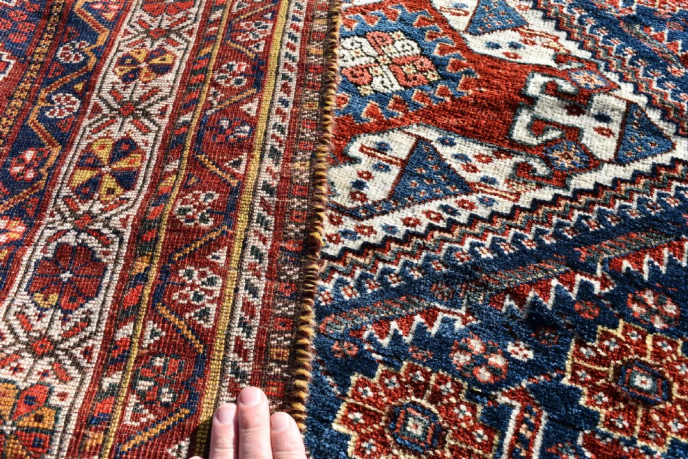 An antique Qashqai tribal wool rug with geometric diamond medallions in navy blue, terracotta red, and cream with fringed edges. View VIII