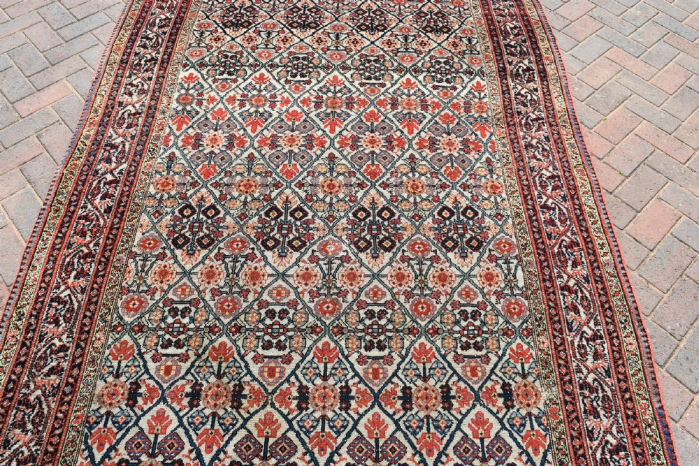 An antique long North West Persian Kelleh carpet featuring an intricate repeating lattice geometric motif in terracotta, navy blue, and cream tones. View V