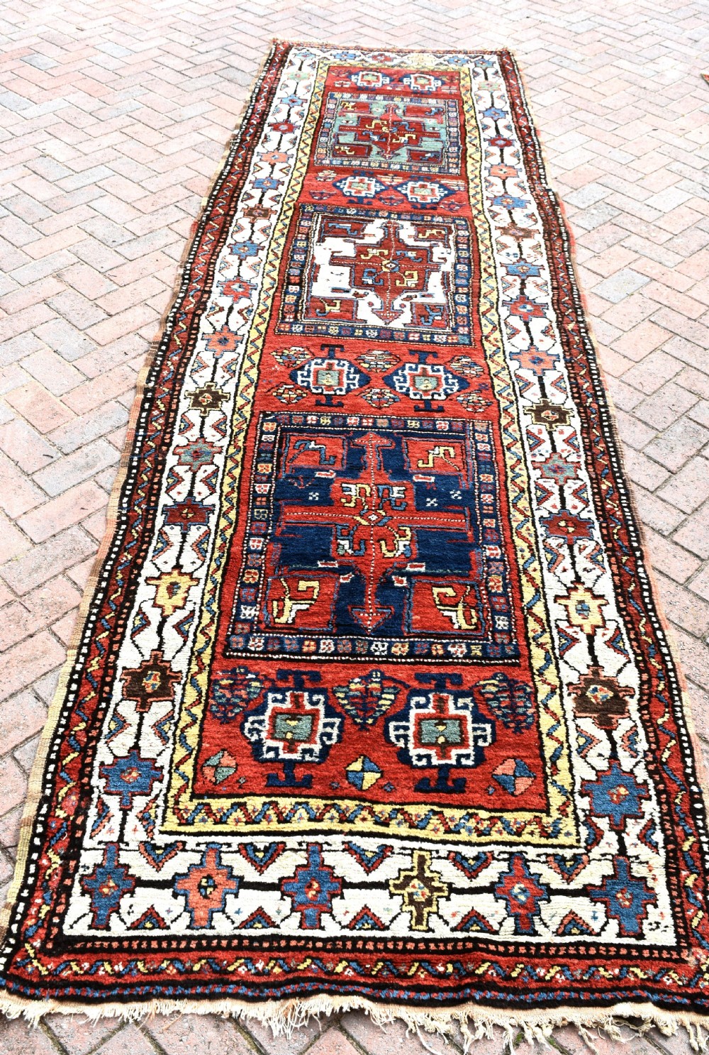 An antique Shahsavan hand-knotted wool long rug featuring geometric medallions in terracotta red, navy blue, yellow, and white.
