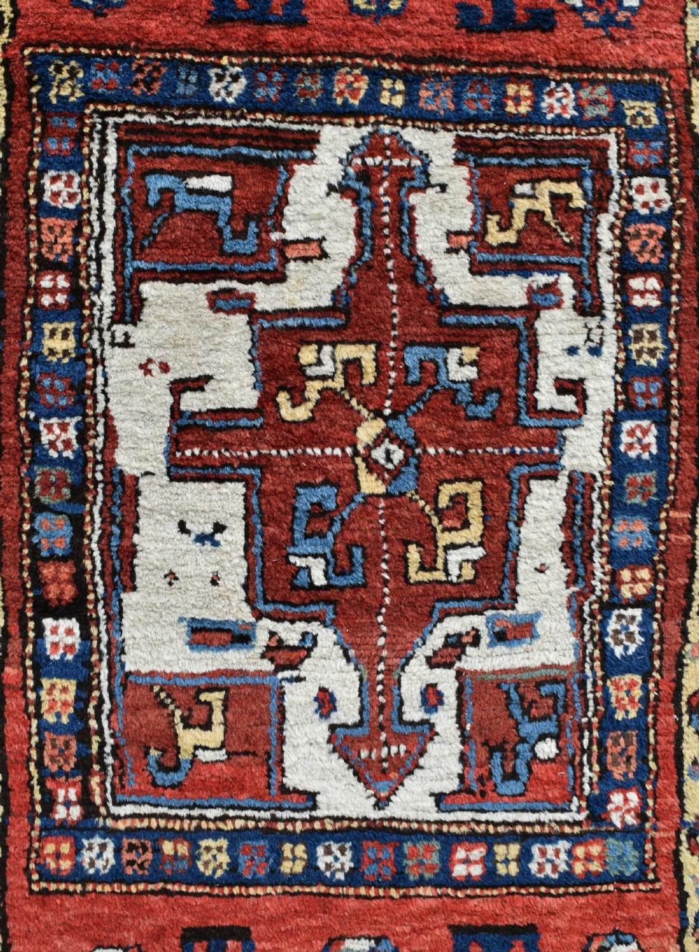 An antique Shahsavan hand-knotted wool long rug featuring geometric medallions in terracotta red, navy blue, yellow, and white. View X