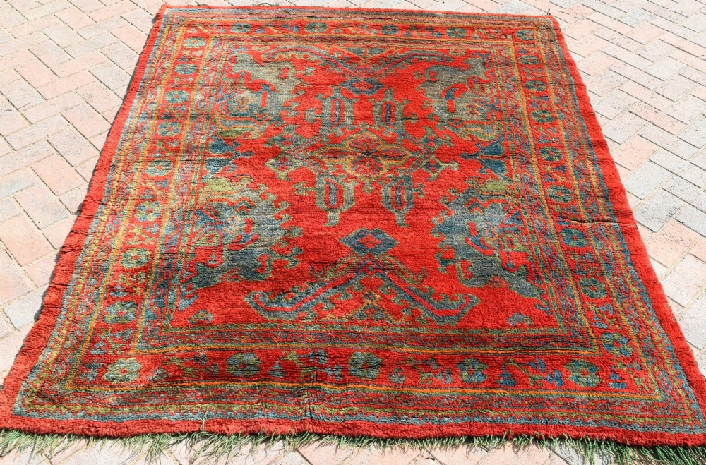 A rectangular hand-knotted antique wool Ushak carpet featuring a vibrant red field with a green and blue central medallion motif and floral borders.