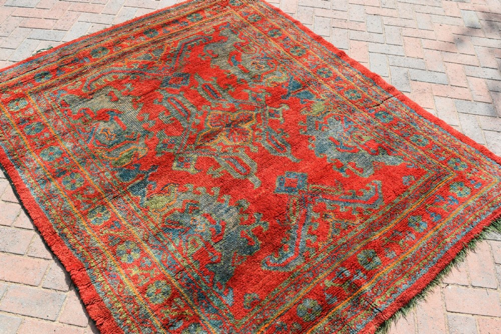 A rectangular hand-knotted antique wool Ushak carpet featuring a vibrant red field with a green and blue central medallion motif and floral borders. View II