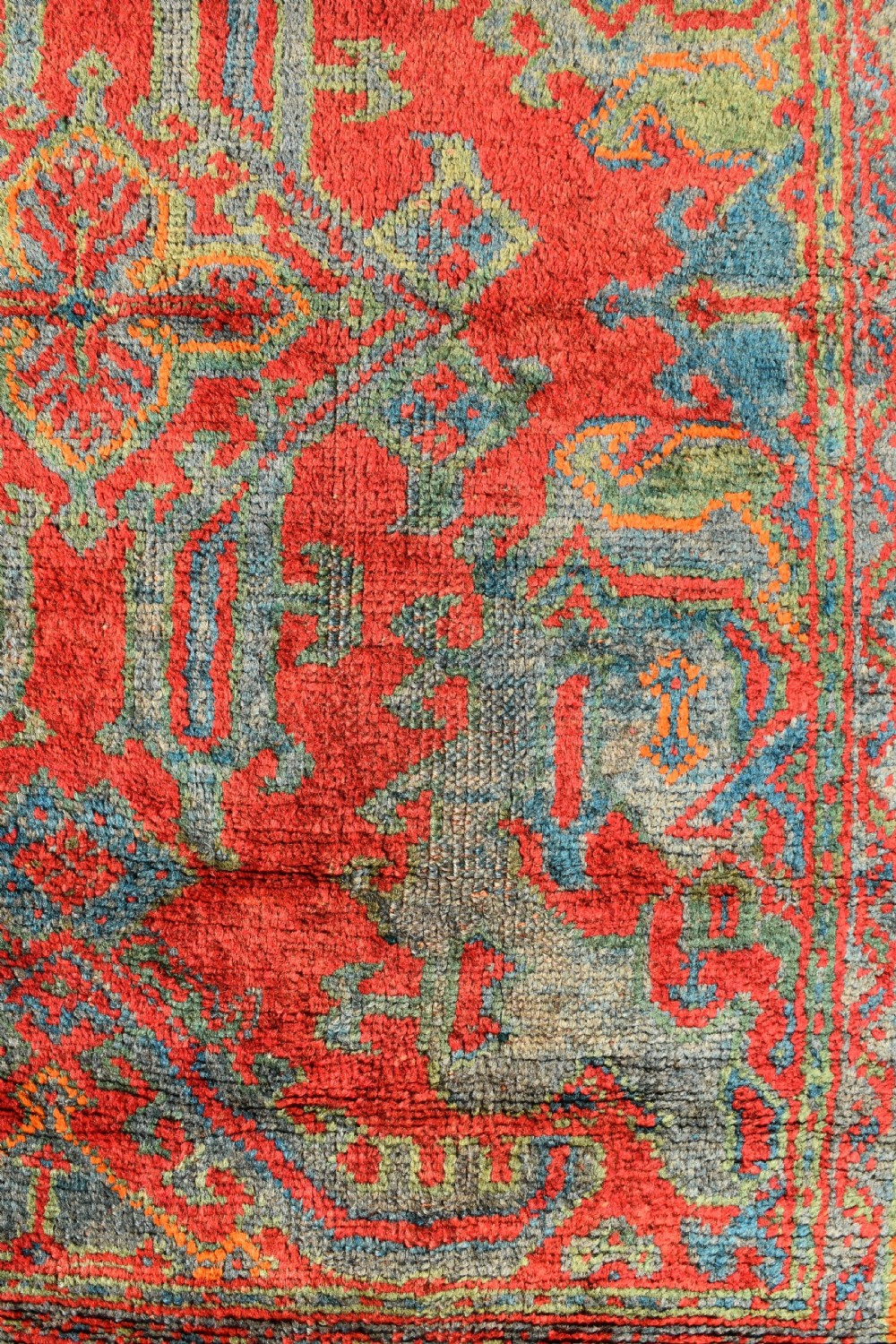 A rectangular hand-knotted antique wool Ushak carpet featuring a vibrant red field with a green and blue central medallion motif and floral borders. View III