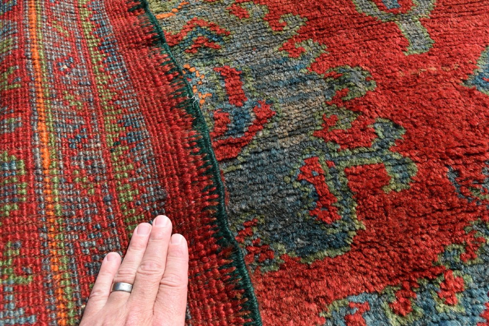 A rectangular hand-knotted antique wool Ushak carpet featuring a vibrant red field with a green and blue central medallion motif and floral borders. View V