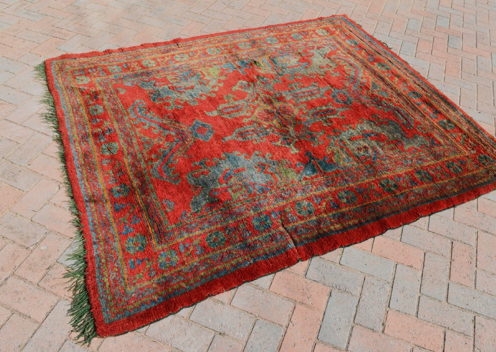 A rectangular hand-knotted antique wool Ushak carpet featuring a vibrant red field with a green and blue central medallion motif and floral borders. View VI