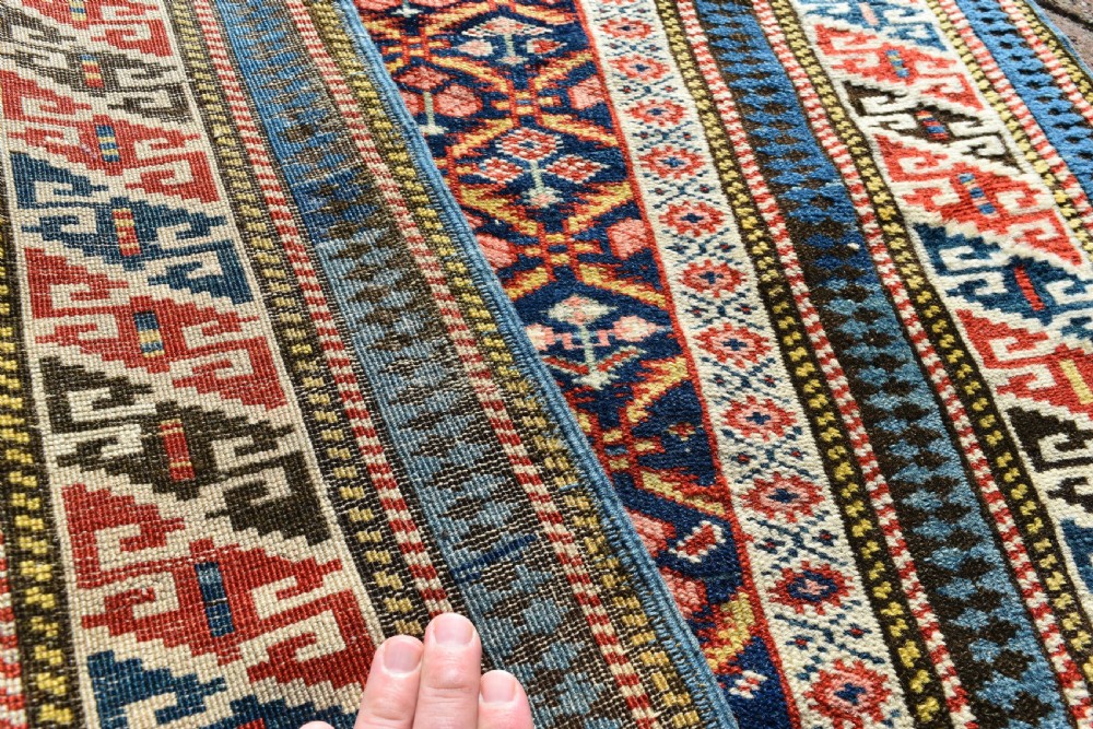 A long, narrow hand-knotted antique Caucasian Kuba runner rug featuring a navy blue geometric diamond lattice pattern framed by intricate multi-coloured borders. View II