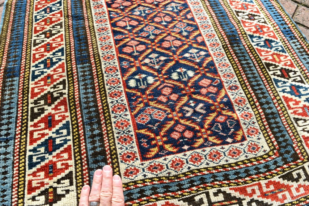 A long, narrow hand-knotted antique Caucasian Kuba runner rug featuring a navy blue geometric diamond lattice pattern framed by intricate multi-coloured borders. View III