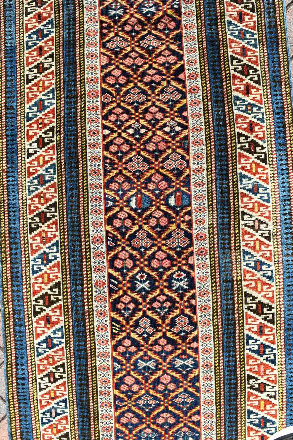 A long, narrow hand-knotted antique Caucasian Kuba runner rug featuring a navy blue geometric diamond lattice pattern framed by intricate multi-coloured borders. View VI