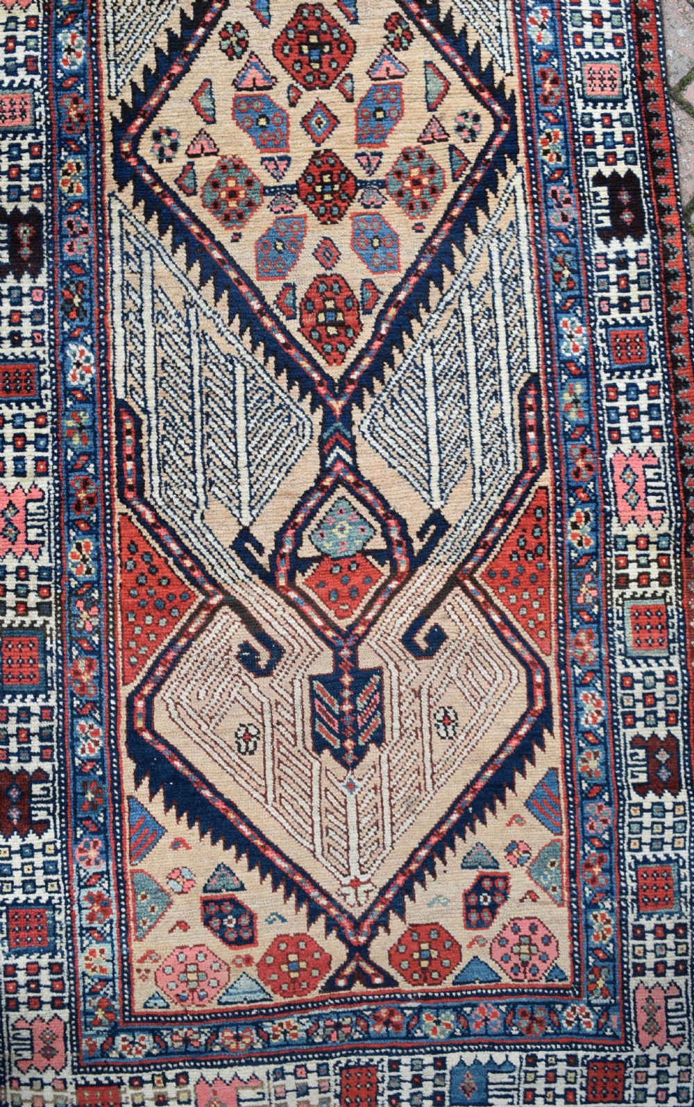 A long, narrow antique hand-knotted Serab wool runner rug featuring repeating geometric diamond medallions in beige, terracotta red, pink, and navy blue tones. View III