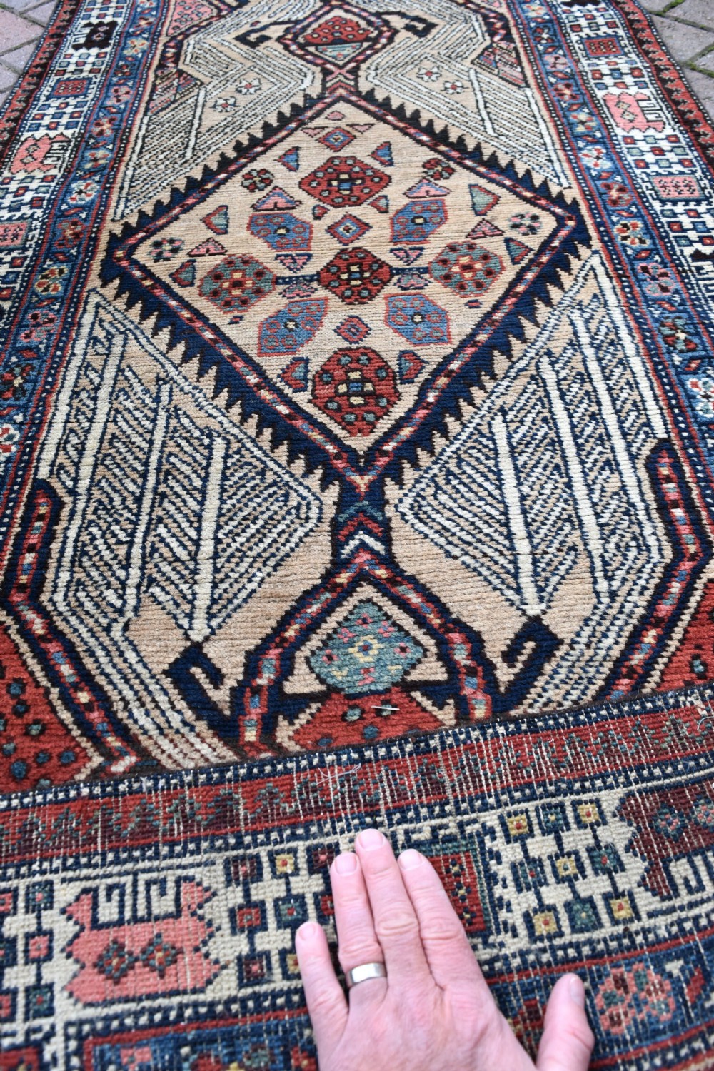 A long, narrow antique hand-knotted Serab wool runner rug featuring repeating geometric diamond medallions in beige, terracotta red, pink, and navy blue tones. View X