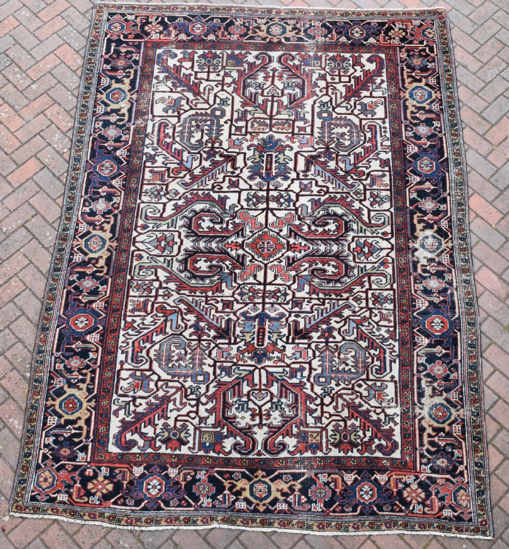 A hand-knotted Heriz wool carpet featuring a large geometric central medallion on an ivory background framed by dark navy floral borders.